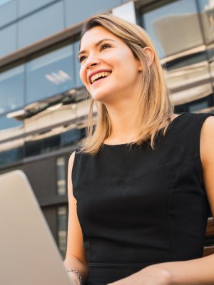 Portrait of young business woman using her laptop while sitting outdoors at the street. Business concept.